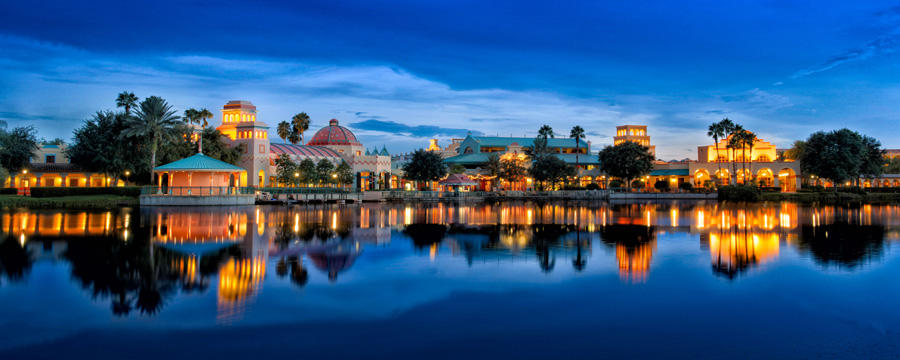 Twilight waterfront view of ornate illuminated buildings reflecting on calm water, warm golden lights against deep blue evening sky